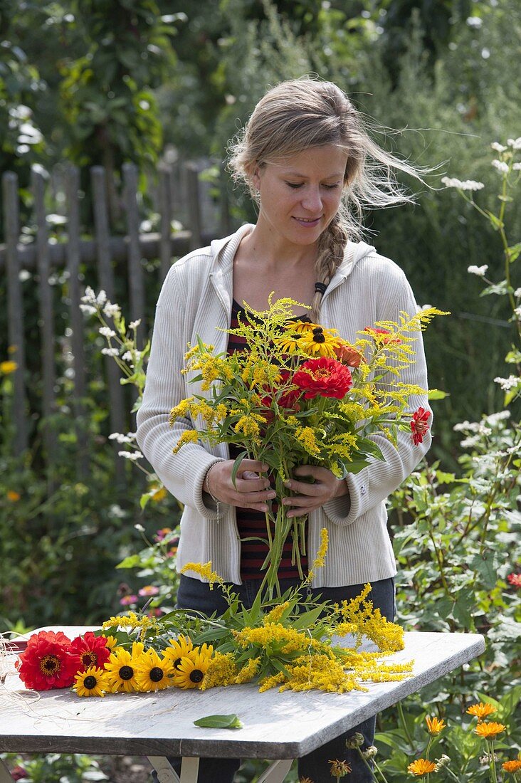 Frau bindet Strauss aus Solidago (Goldrute), Zinnia (Zinnien) und Rudbeckia