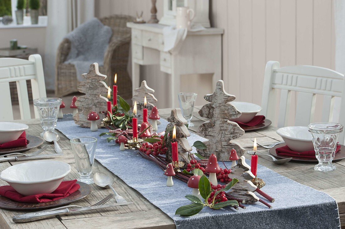 Gedeckter Tisch mit kleinen Weihnachtsbaeumen aus Birkenrinde, roten Beeren