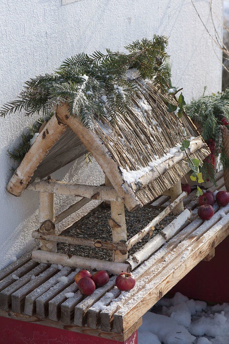 Birdhouse made of birch with straw roof and fir branches on the terrace