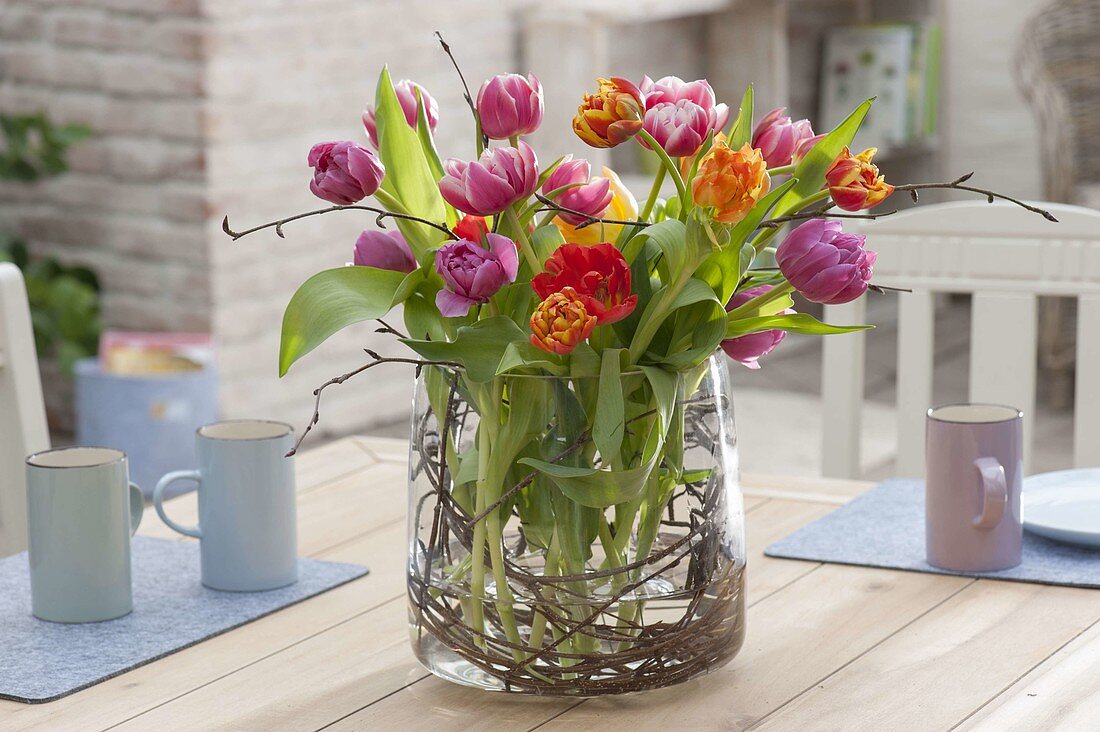 Strauss aus gefuellten Tulipa (Tulpen) in breitem Glas mit Zweigen von Betula