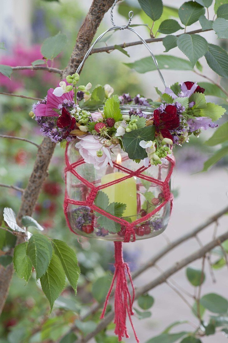 Preserving jar with macrame as lantern on tree, wreath of tropaeolum