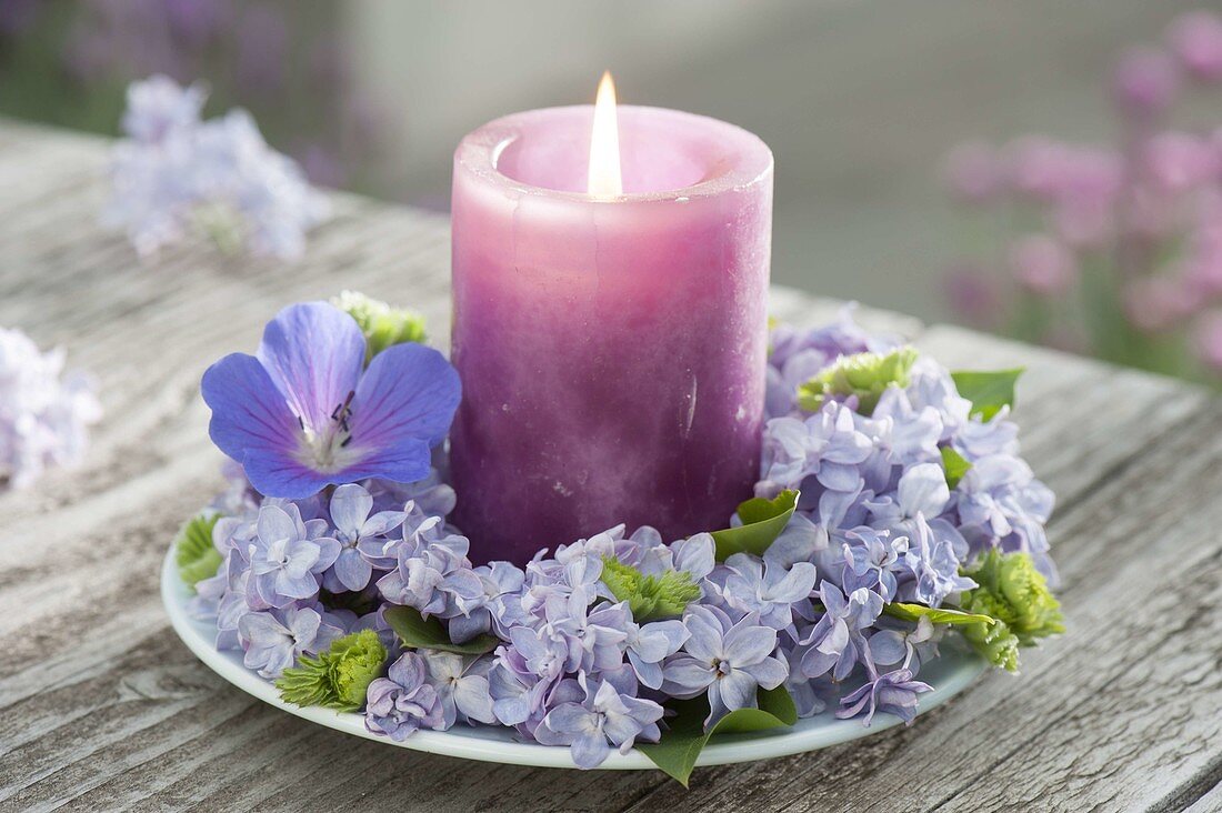 Kerze in Kranz aus Syringa (Flieder) mit einer Blüte von Geranium