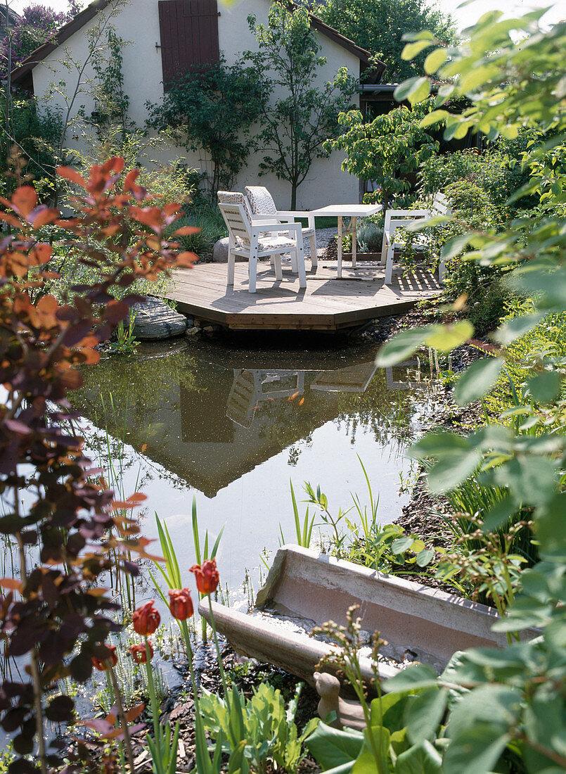 Holzterrasse mit weißen Gartenmöbeln am Teich