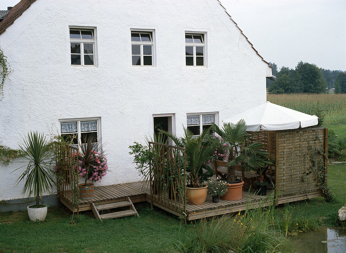 Holzterrasse am Haus neben Teich, Sichtschutzwand, Sonnenschirm