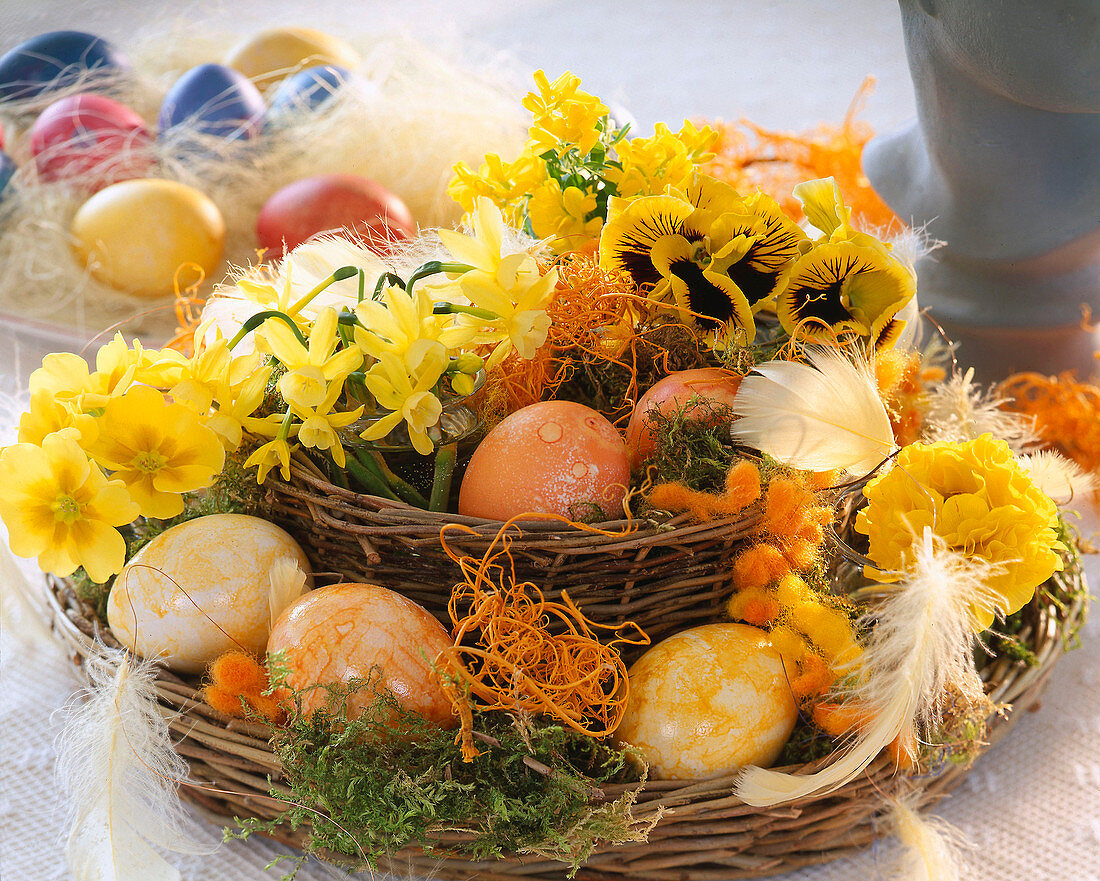 Weidenkorbetagere mit bemalten Eiern, Narzissenblüten, Primeln, Stiefmütterchen