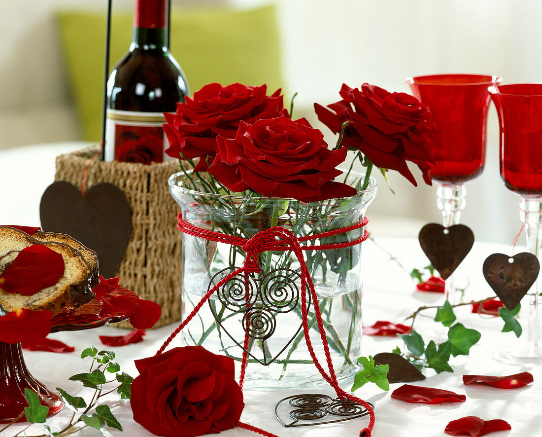 Red rose blossoms in a glass with wine glasses