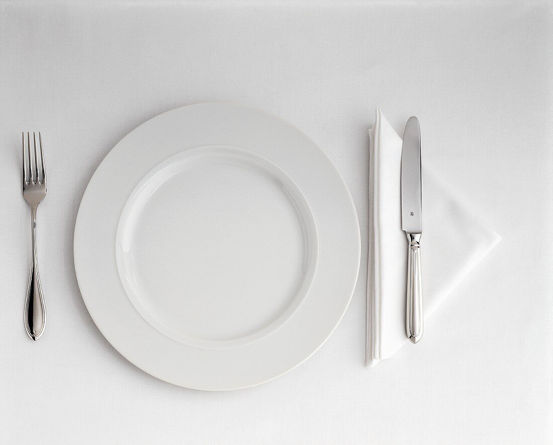 Ein Gedeck mit weißem Teller, Besteck & dreieckiger Serviette