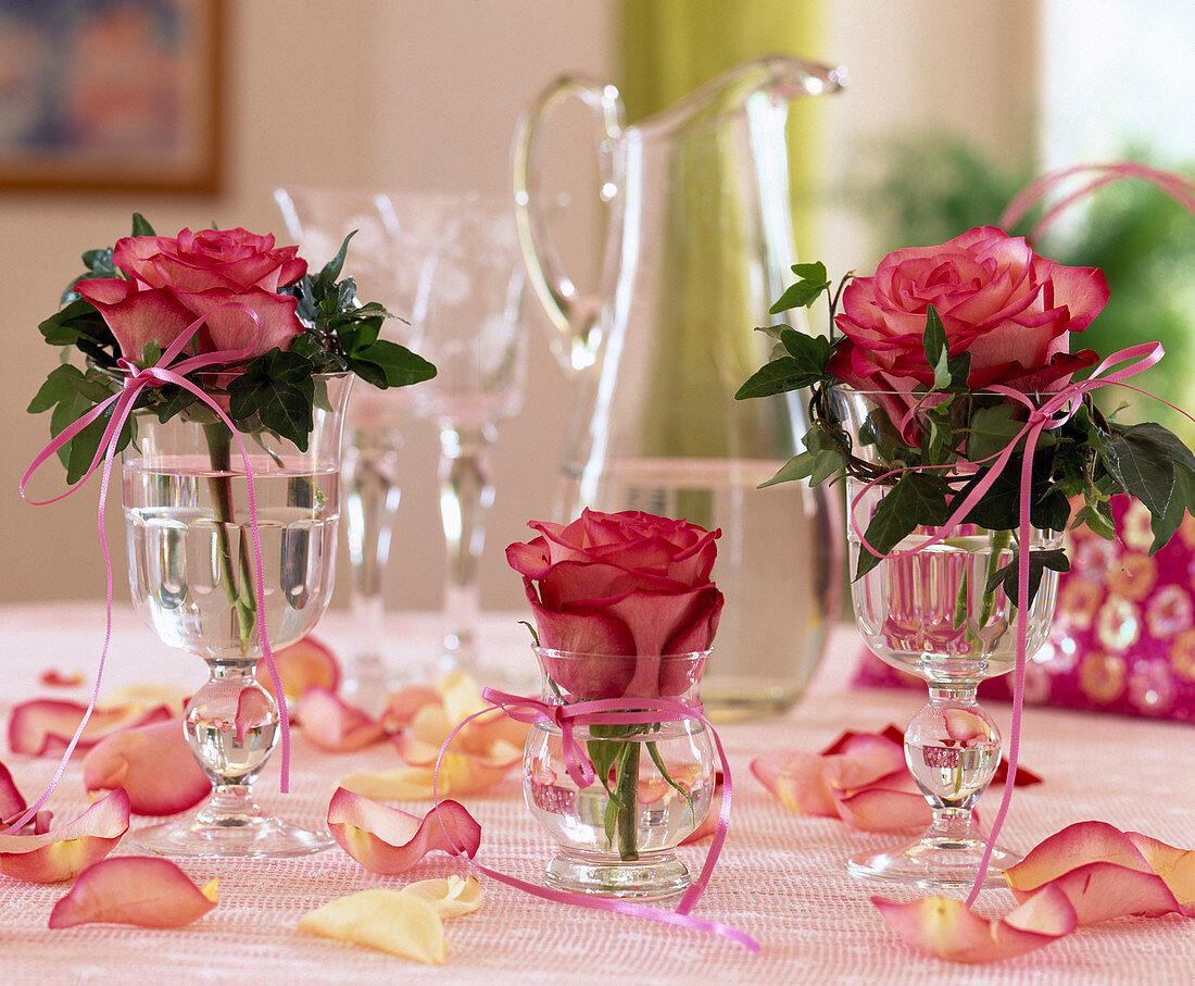 Rose flowers individually in glasses decorated with ribbons and ivy
