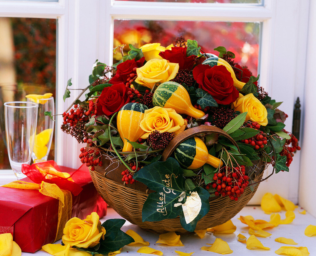 Korb mit Herbstgesteck aus Rosen, Zierkürbissen und Beerenschmuck