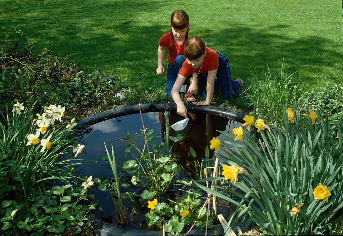 Children playing with paper boats at the pond