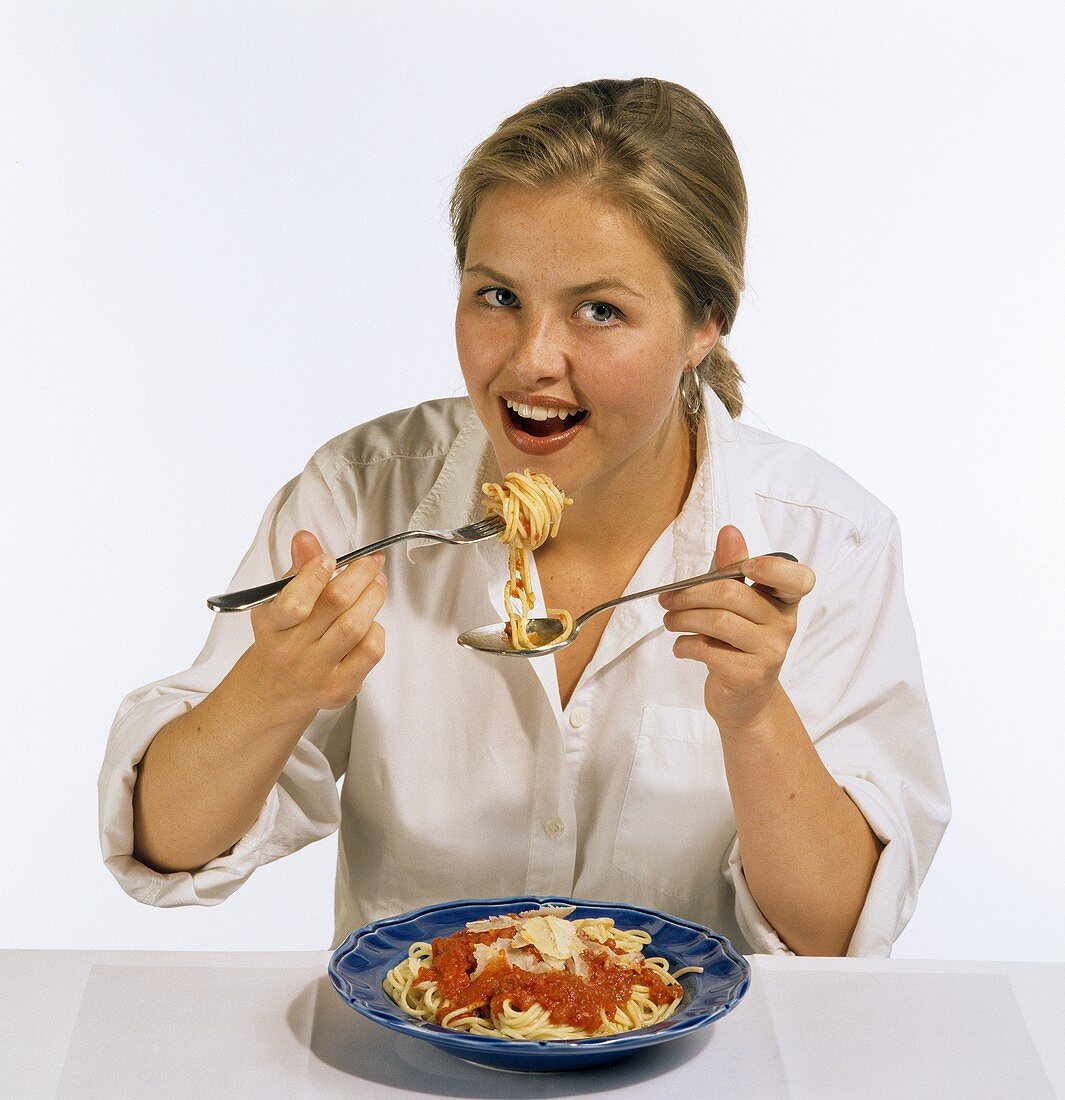 Modell frisst Spaghetti mit Tomatensauce von einem blauen Teller
