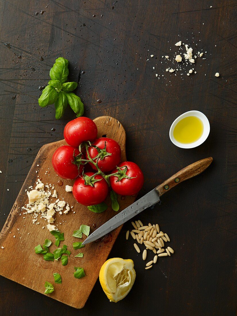 Tomaten, Basilikum und Parmesan auf Holzbrett, danben Zitrone, Pinienkerne und Olivenöl