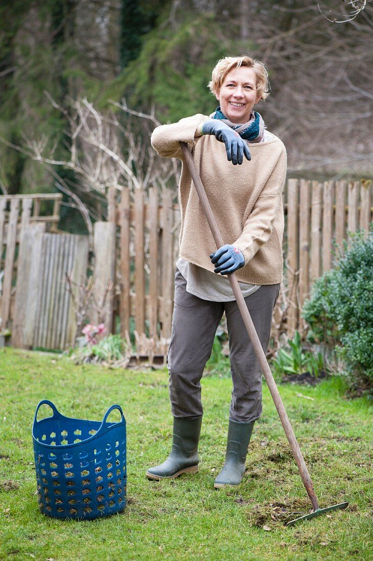 Woman removing thatch from lawn leaning on rake