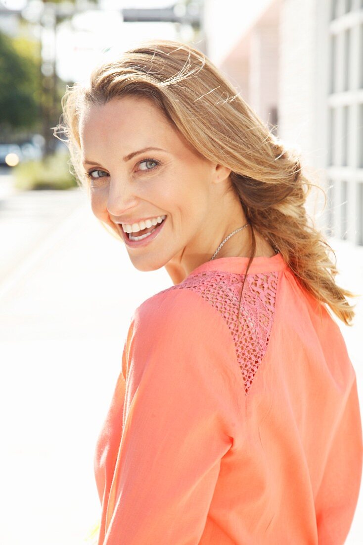 Blonde woman wearing coral-pink blouse with lacy inserts