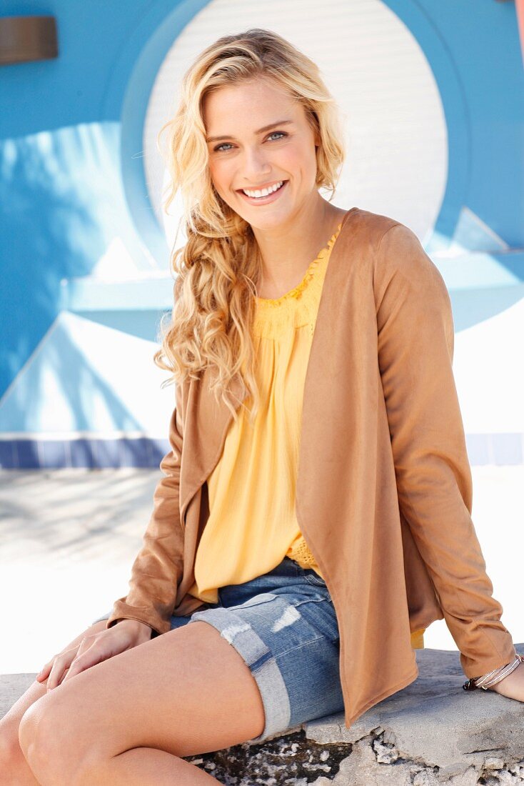 Blonde woman wearing yellow top, denim shorts and brown velour cardigan