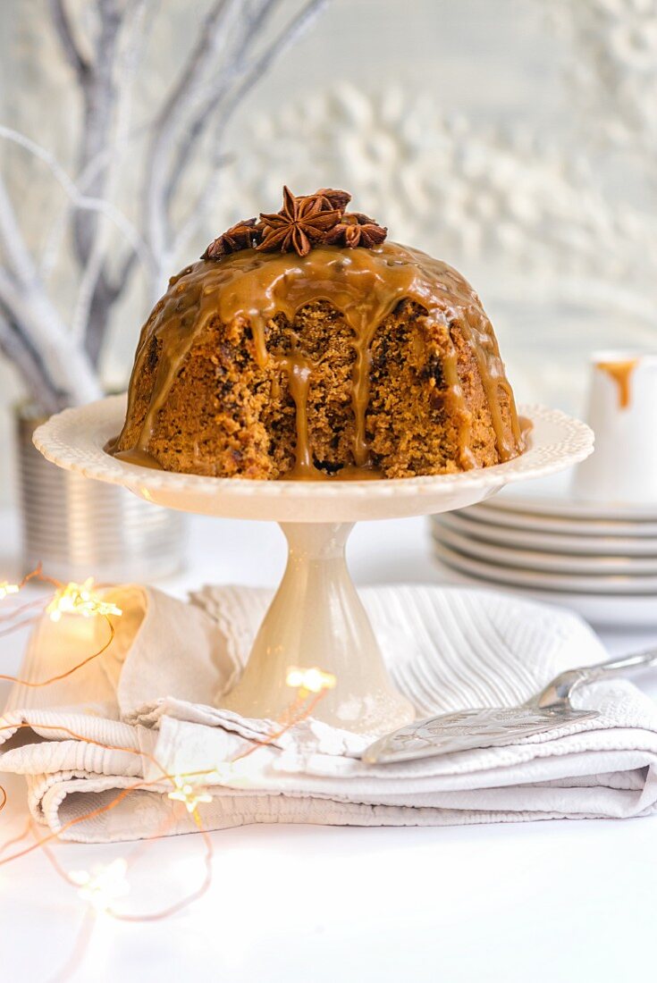 Steamed ginger and date pudding drizzled with toffee sauce and decorated with star anise on a cake stand