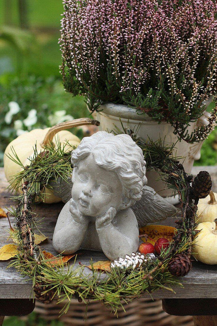 Stone cherub in small larch wreath next to heather