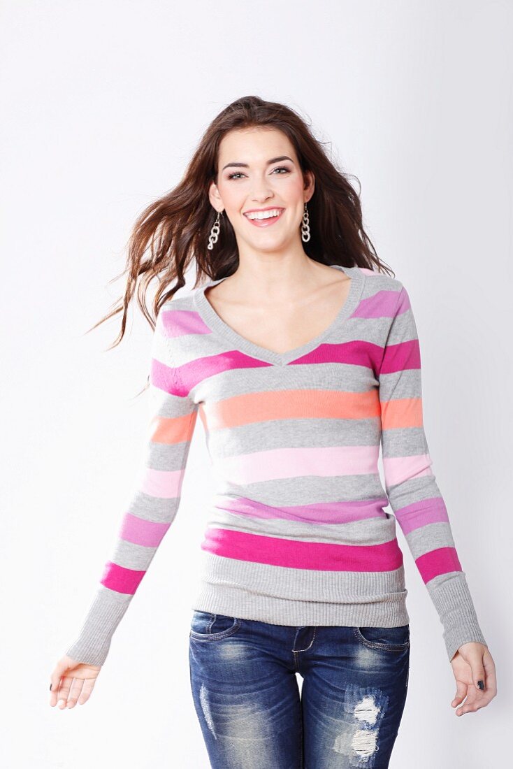 A brunette woman wearing a brightly striped V-neck jumper and jeans