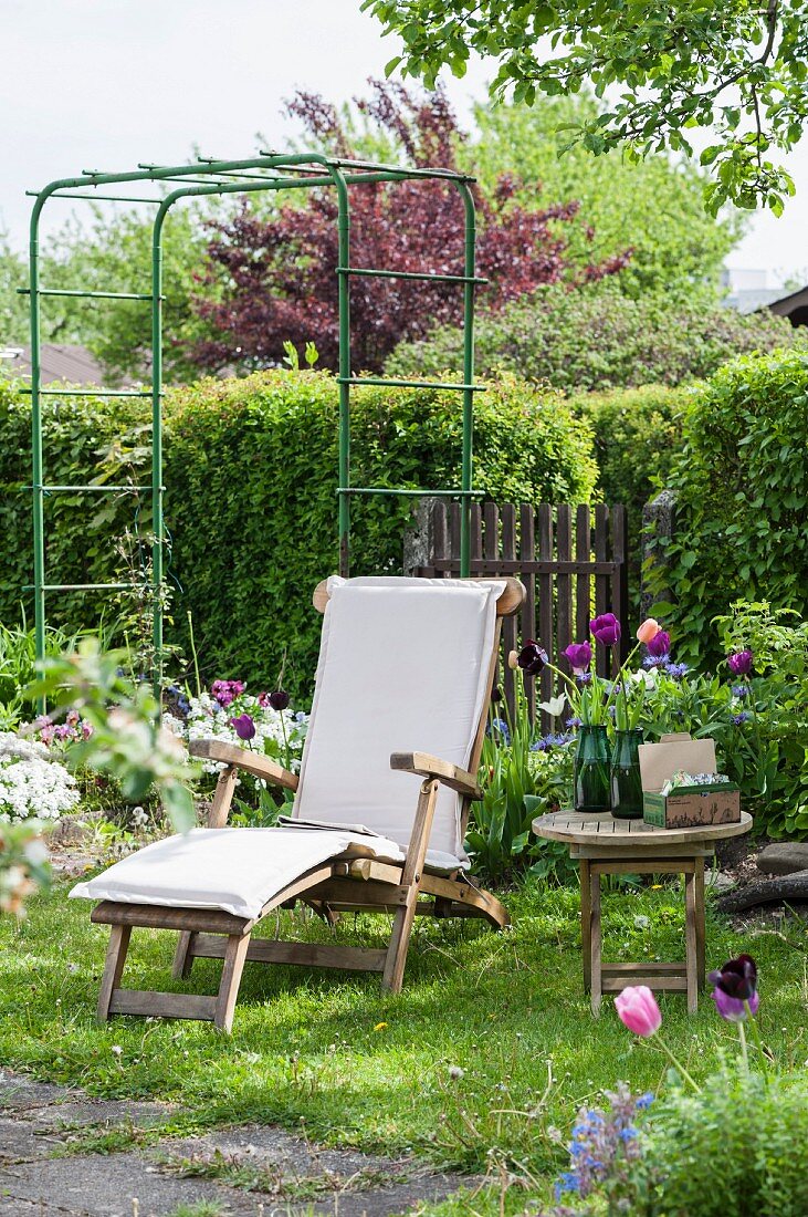 Holzliegestuhl, blühende Tulpen und Rankgerüst im Garten