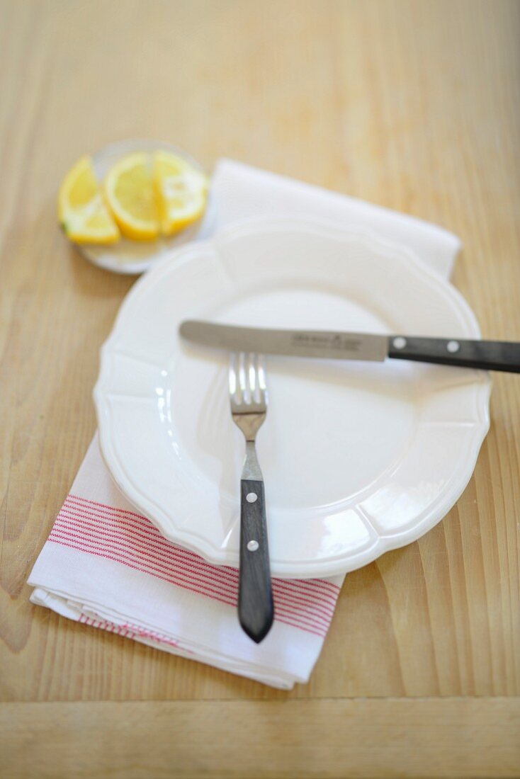 A plate with a knife and fork on a kitchen towel, with lemon slices in the background