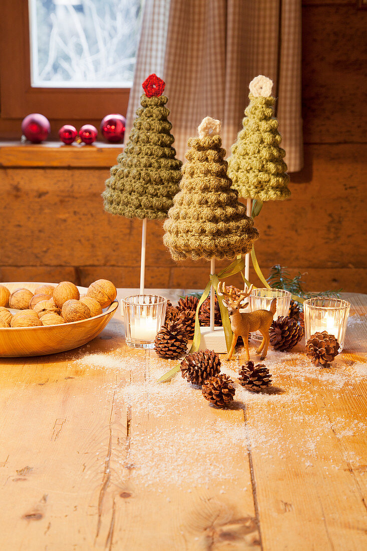 Gehäkelte Weihnachtsbäumchen und Windlichter auf dem Holztisch