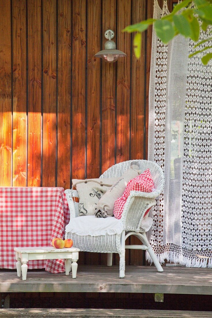 Cushions on white wicker armchair on wooden terrace