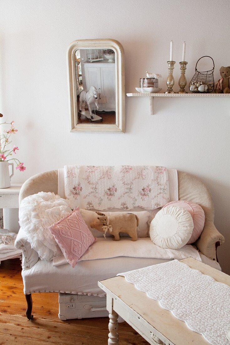 Sofa mit Kissen und Schweinchenfigur unter Wandspiegel in Shabby Stil