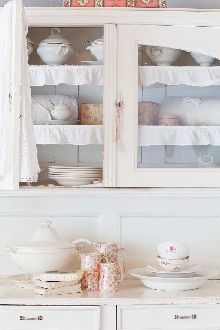 Crockery in shabby-chic dresser with glass-fronted upper section and open glass door