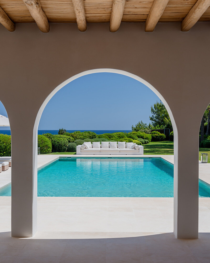 View of pool and long outdoor sofa seen through archades