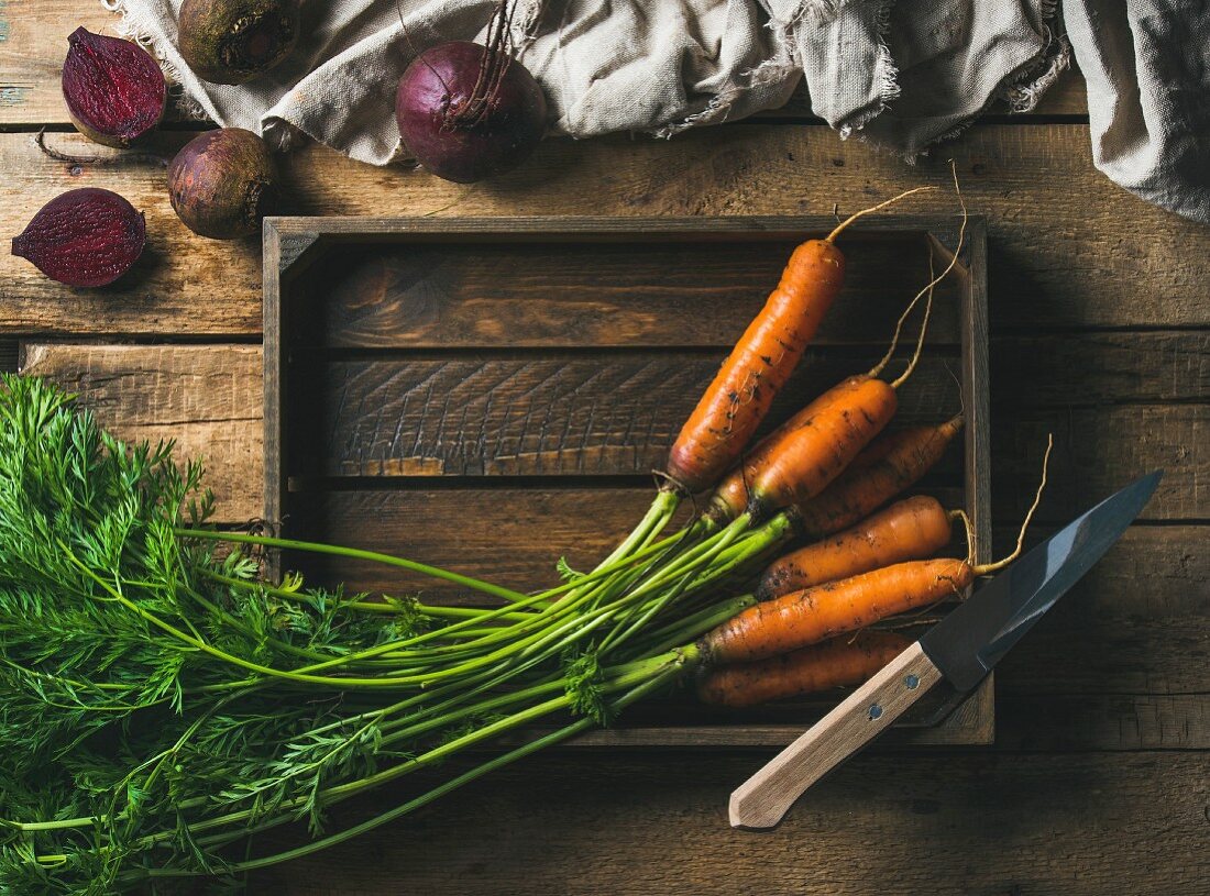 Fresh garden carrots in a wooden tray and beetroots against a rustic wooden background