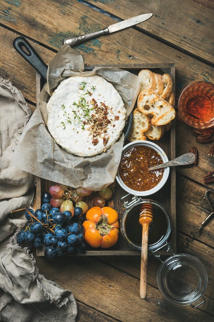 Camembert in kleinem Topf, Trauben, Khaki, Feigenmarmelade, Honig, Baguettescheiben und ein Glas Roséwein