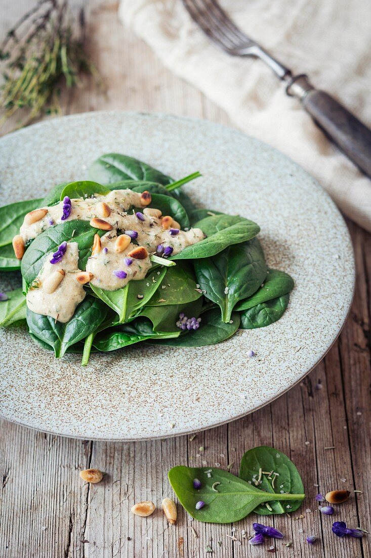 Veganer Spinatsalat mit Knoblauchdressing, Pinienkernen und Essblüten
