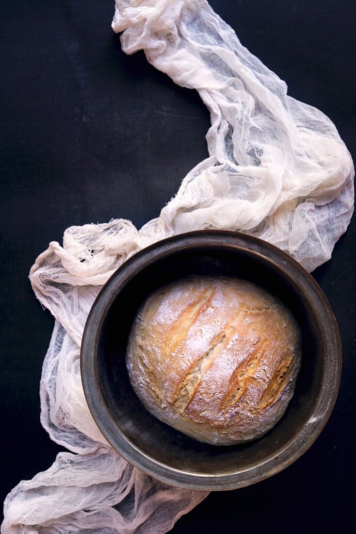 A loaf of bread in a baking tin on a cheesecloth