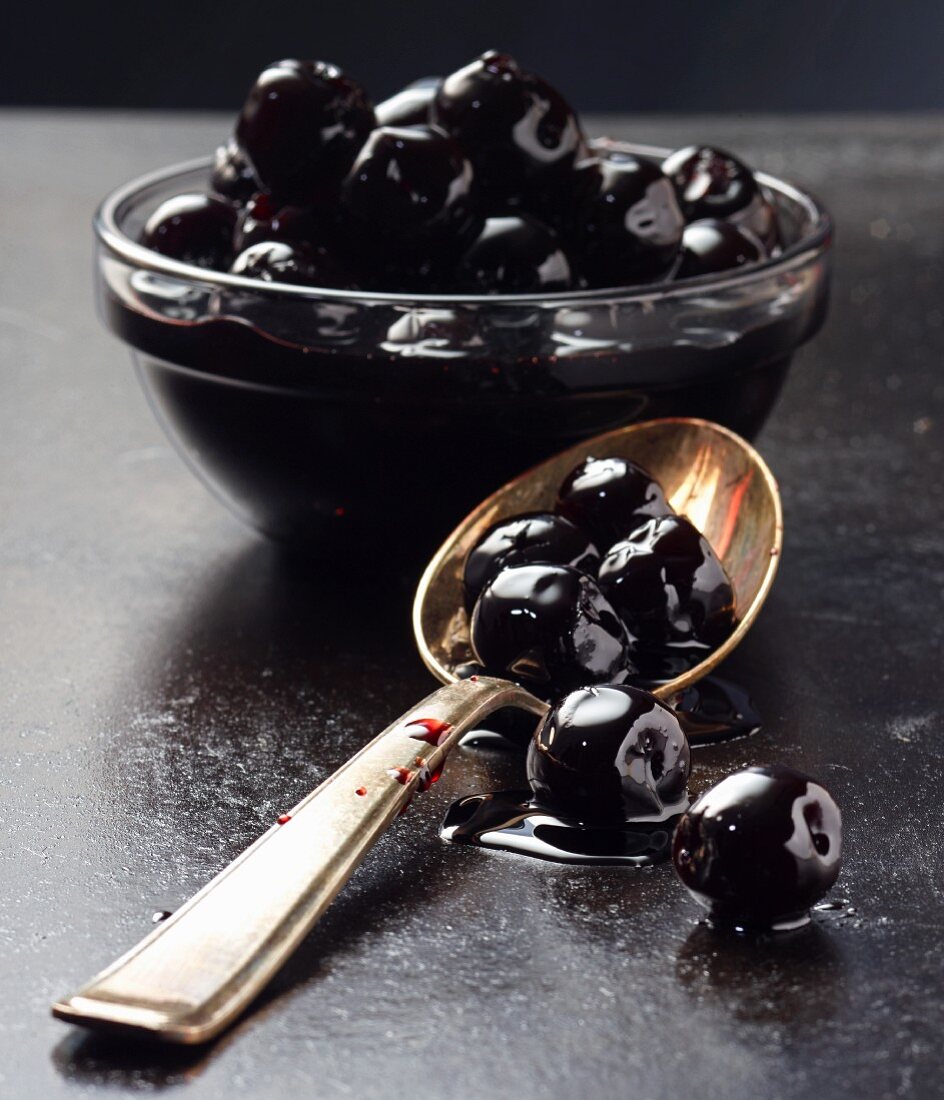 Black olives in a glass bowl and on a spoon