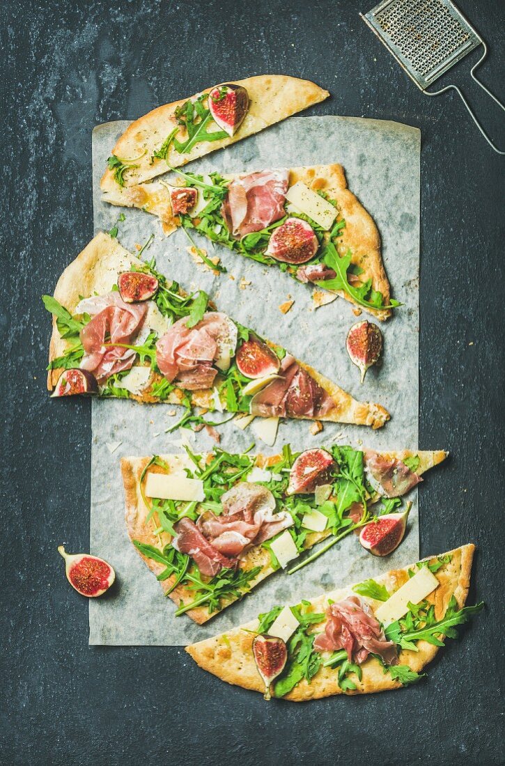 Fig, prosciutto, arugula and sage flatbread pizza cut into pieces on baking paper