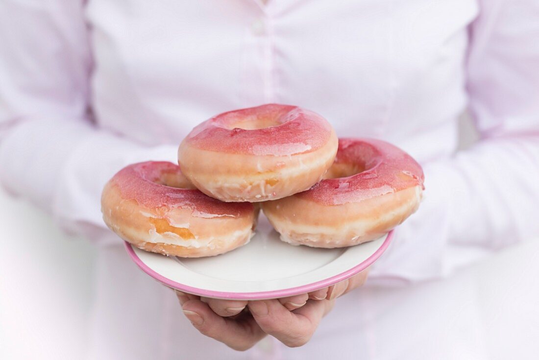A woman holding a plate of pink glazed donuts