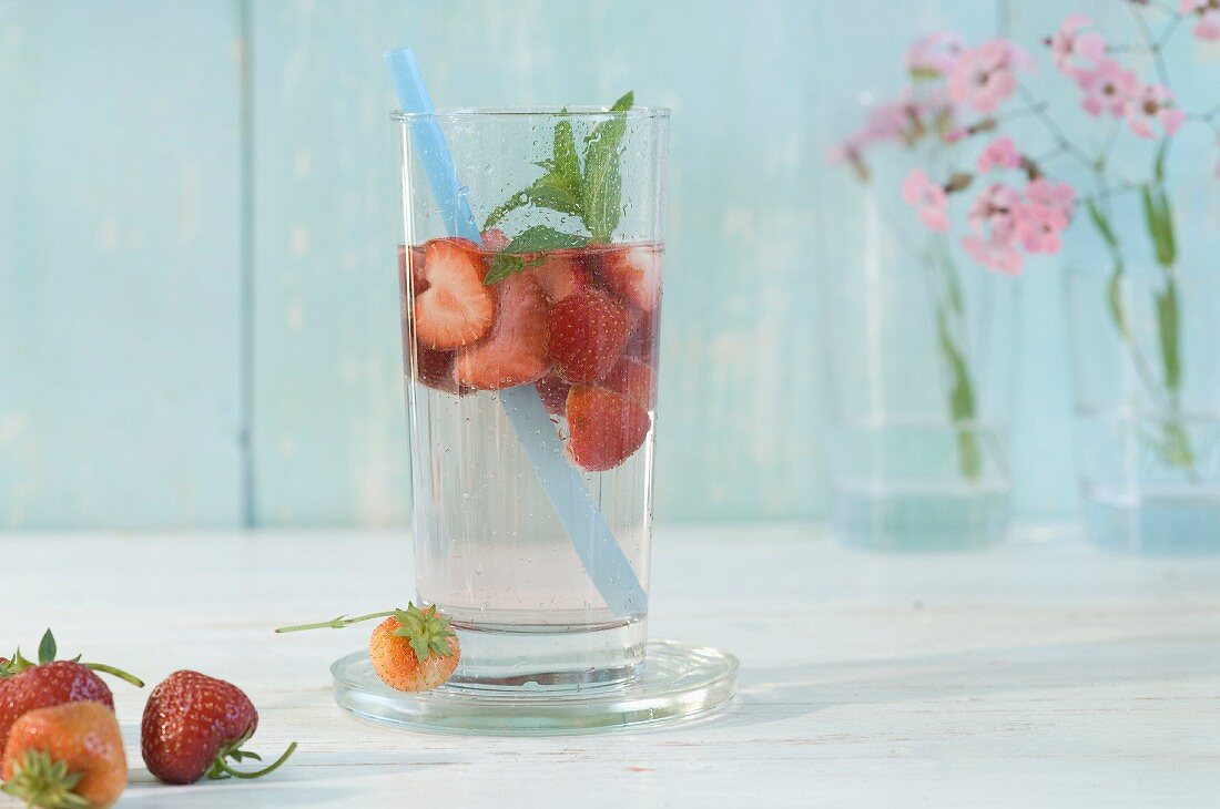 Mit Erdbeeren und Pfefferminze aromatisiertes Wasser im Glas mit Trinkhalm