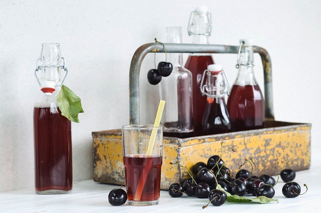 Cherry juice in a glass with a straw, bottles in a bottle carrier and fresh cherries