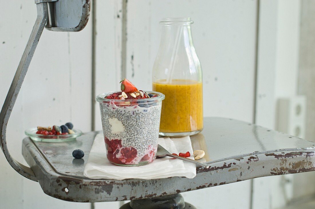 A chia pudding with summer fruits and nuts in a glass and a mango and orange smoothie with chia seeds on an old chair
