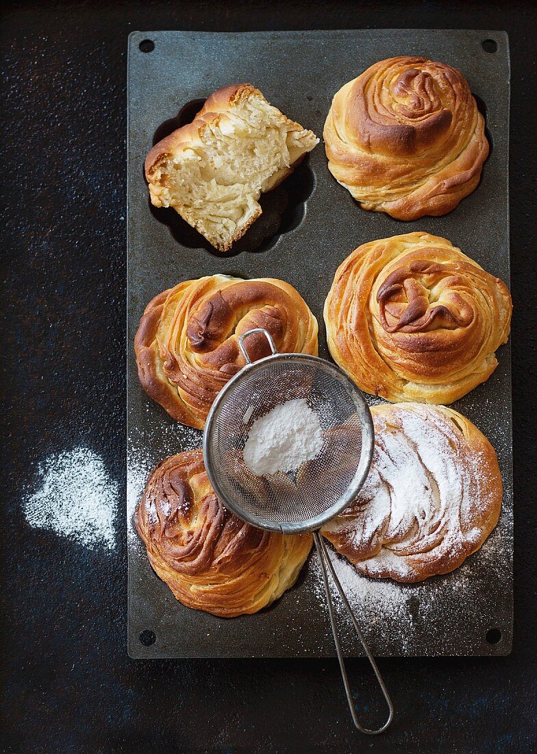 Fresh baked modern pastries cruffins, with sugar powder served in silicon baking form with sieve