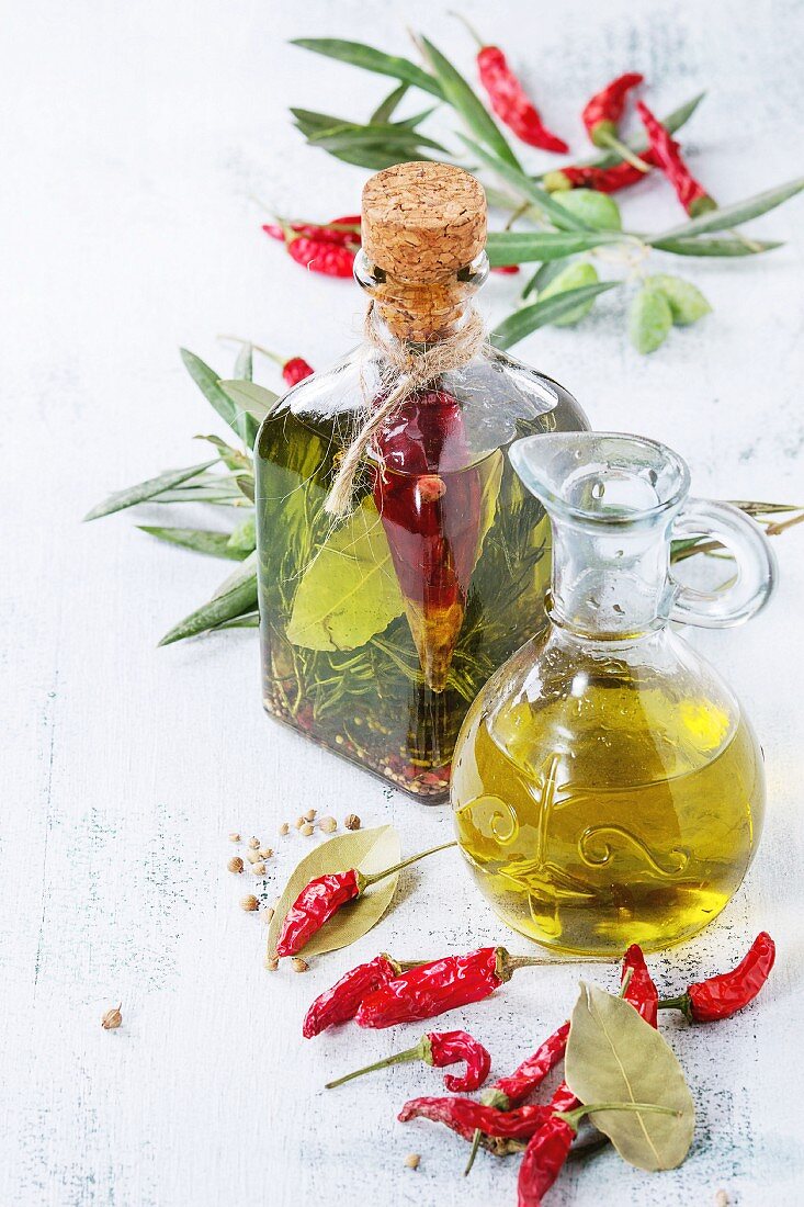 Glass bottle and jug of spicy olive oil with rosemary, red hot chili peppers and bay leaf