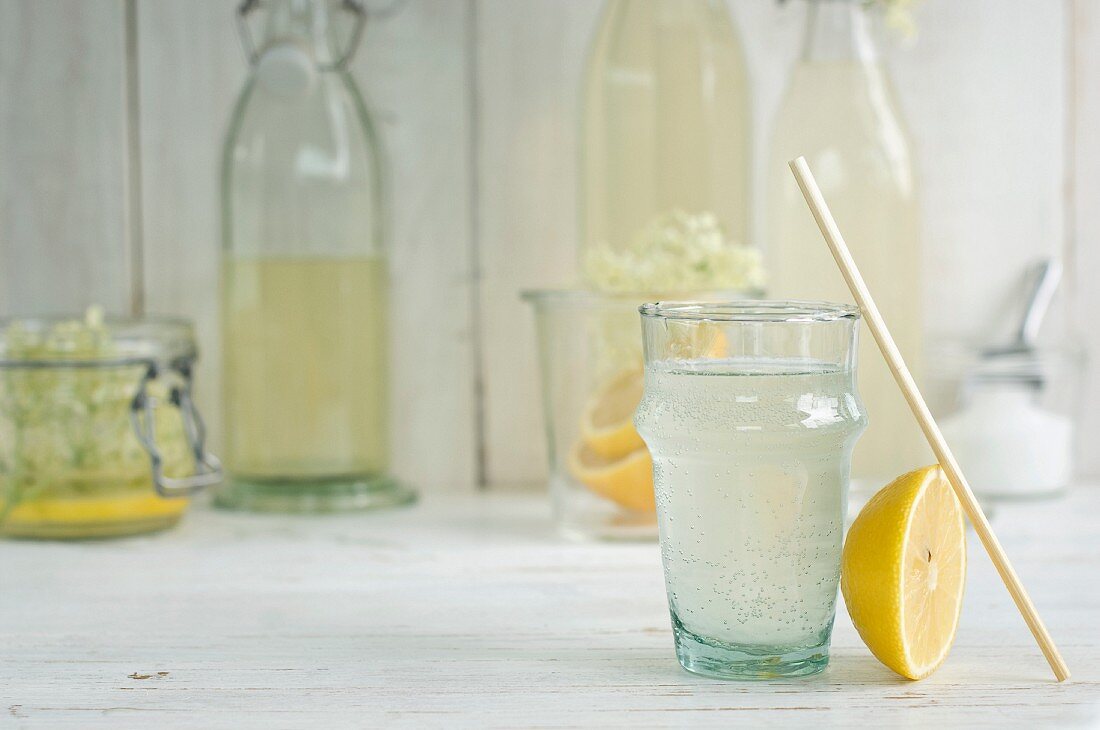 Holunderblütengetränk im Glas mit Trinkhalm und selbstgemachter Holunderblütensirup in Flaschen