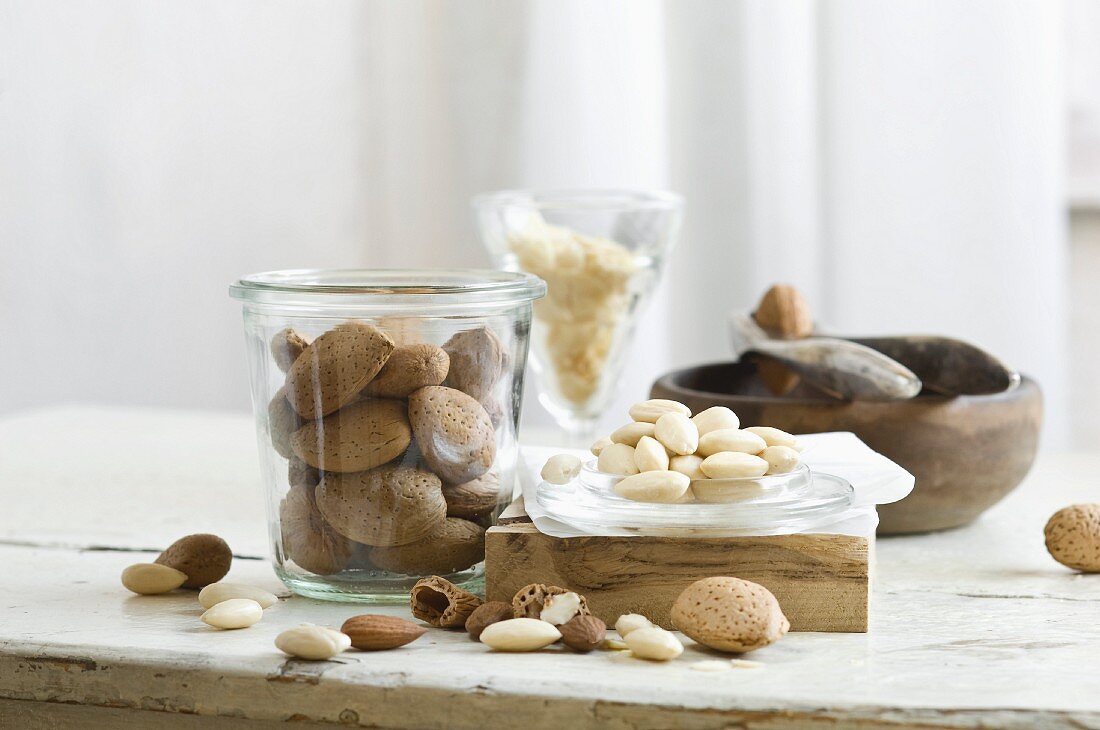 Almonds in and next to a glass jar and a nutcracker on a rustic kitchen table