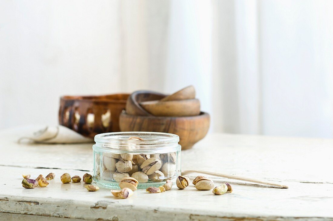 Pistachios in and next to a glass jar on a rustic kitchen table