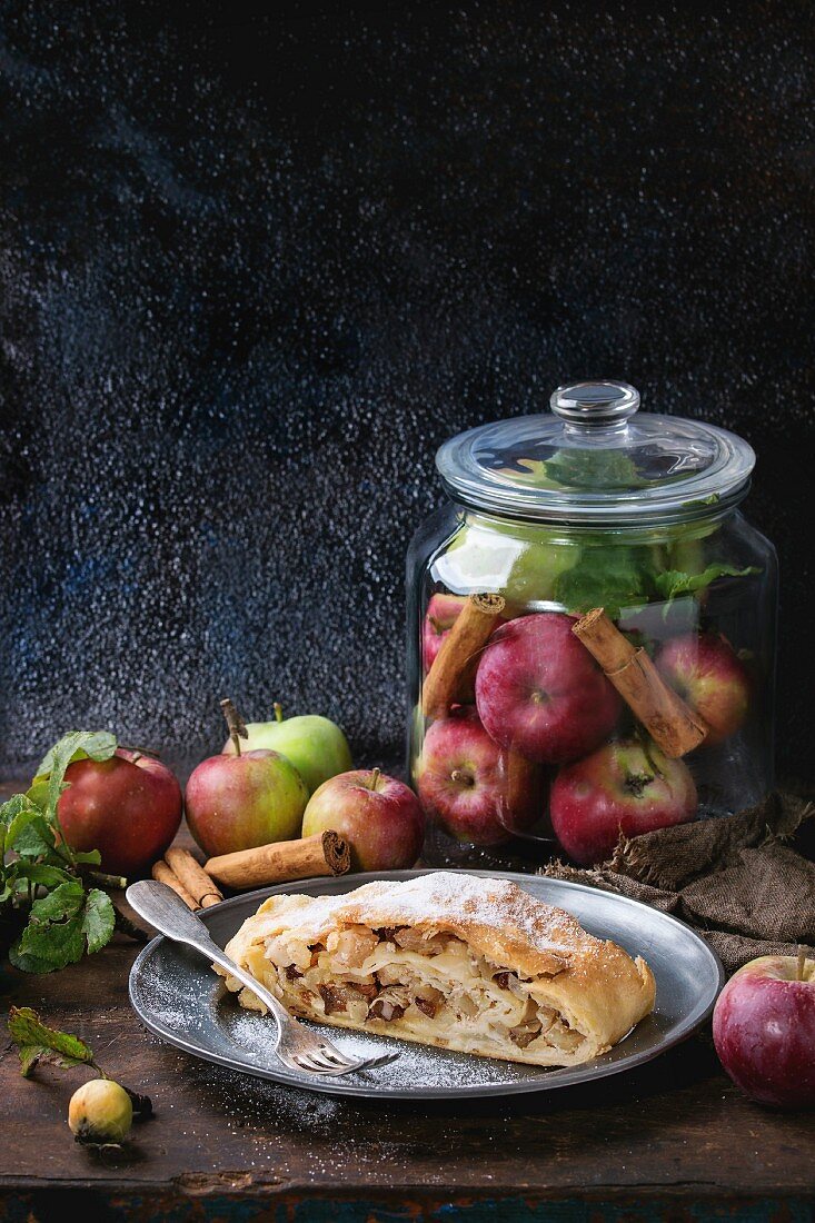 Sliced homemade apple strudel served with fresh apples in glass jar