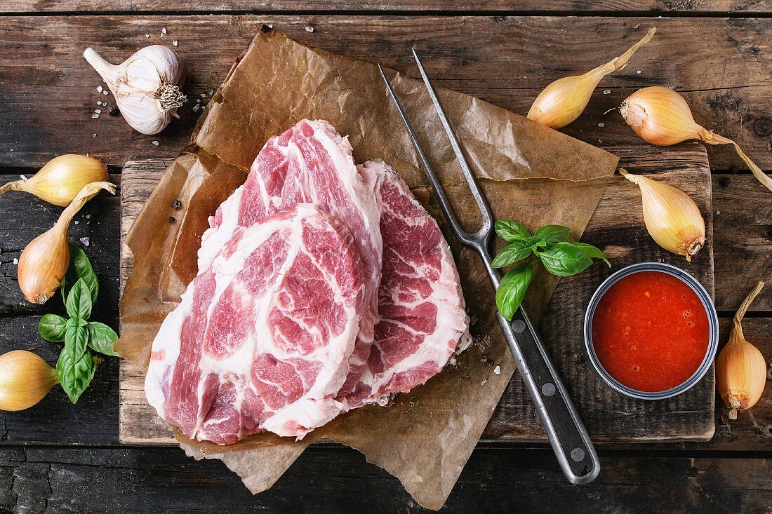 Raw steak meat pork neck on chopping board with shallot onion, tomato sauce marinade, basil and seasoning