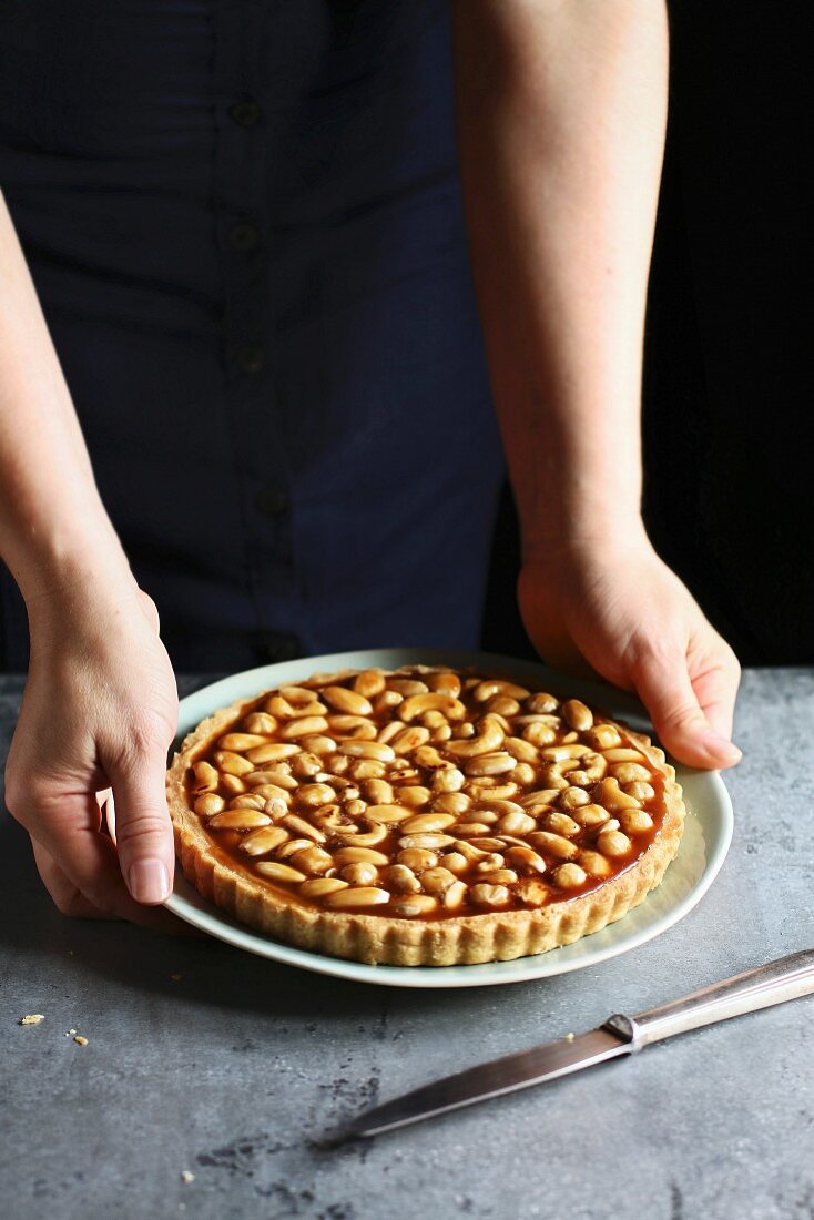 Female hands holding a caramel nut tart on a plate