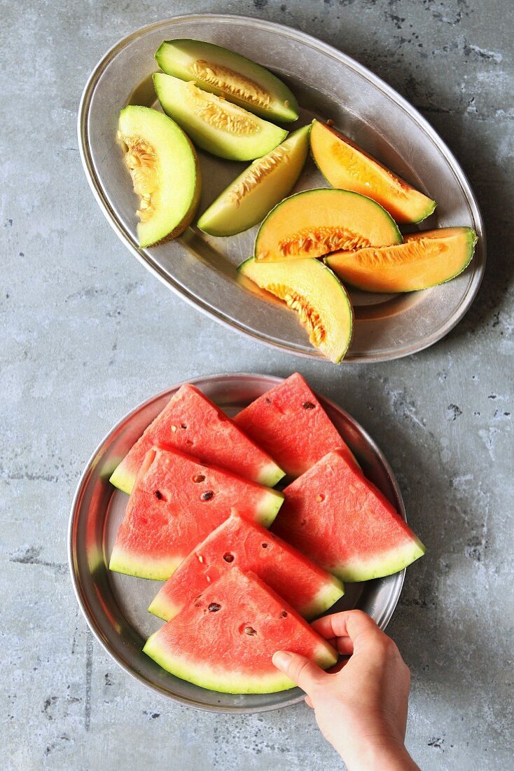 Frisch geschnittene Melonen auf Platten, Frauenhand hält ein Stück Wassermelone