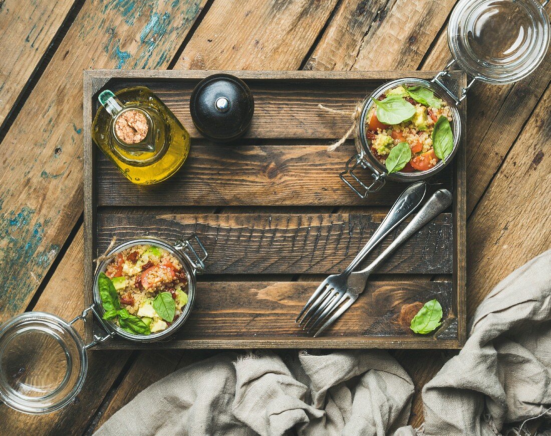 Healthy homemade glass jar quinoa salad with sun-dried Cherrytomatoes, avocado, basil in wooden box