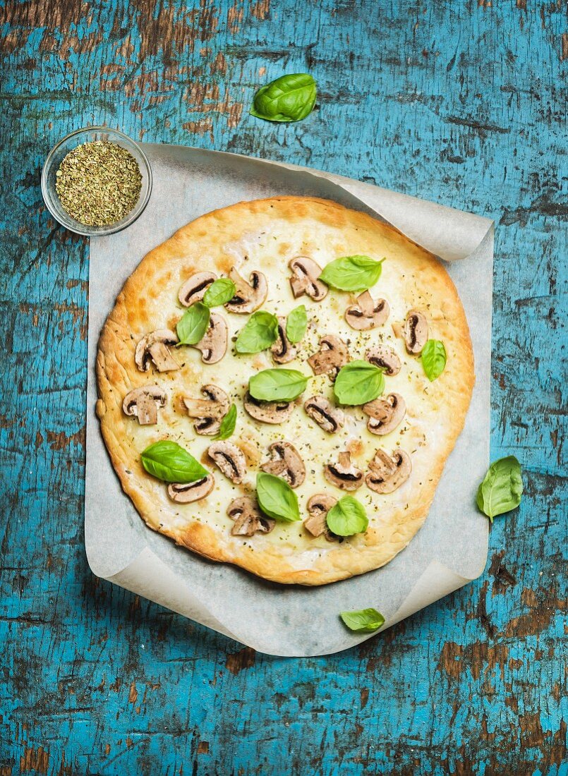 Homemade mushroom pizza with basil leaves and spices in glass on baking paper